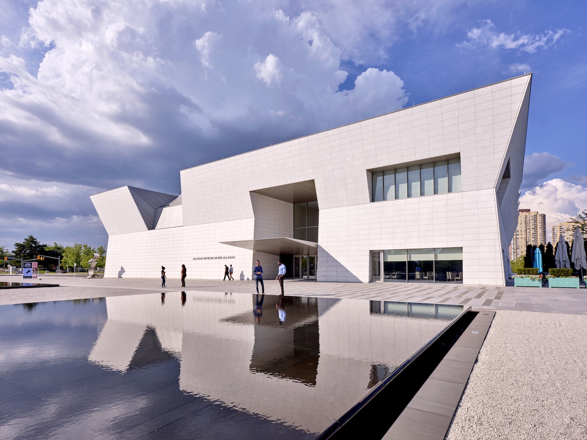 The front exterior of the Aga Khan Museum is reflected in a shallow pool